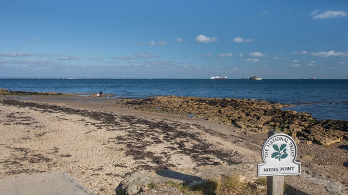 A National Trust omega sign invites visitors onto Nodes Point beach, a mixture of sand and pebbles and rocks which are ideal for rockpooling